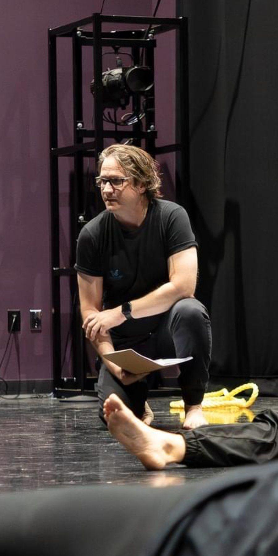 Josh Pohja kneeling with script in hand during rehearsal