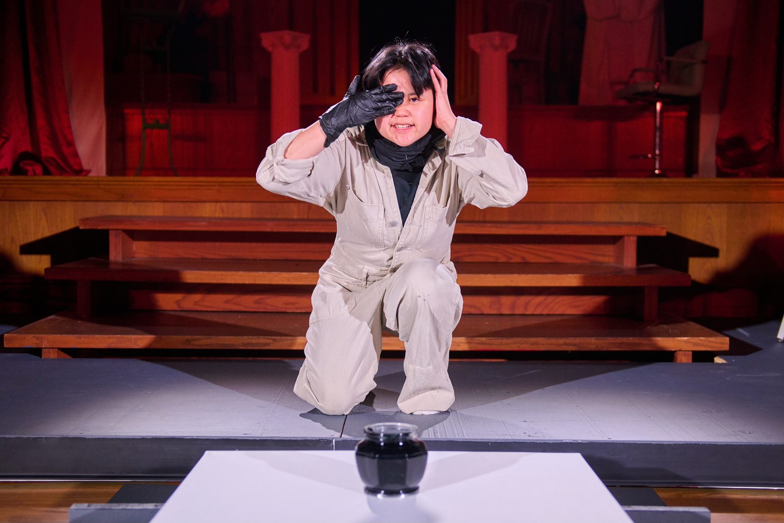 A performer kneeling alone on stage in Wisconsin Classic Stage's production of The Persians